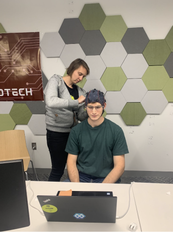 A researcher placing the unicorn cap on a test subject. One test subject had to close their eyes for one minute, open their eyes for another, and then solve a difficult math problem in their head. The brain waves the researcher collected were then generated into imagery. 